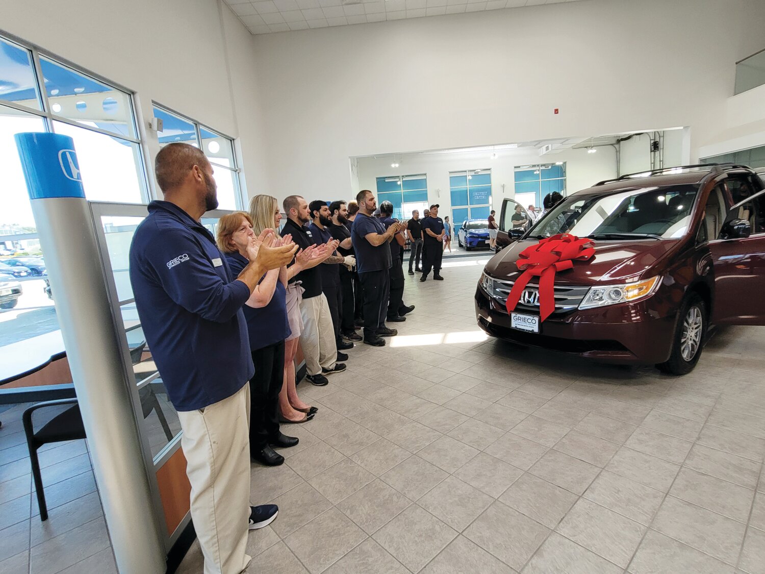 EMPLOYEE INVESTMENT: Grieco Automotive Group’s employees lined up in Grieco Honda’s huge Johnston showroom, awaiting the day’s guest-of-honor, Ciarra Muller. The dealership presented Muller’s family with a wheelchair-accessible van and a check for $3,000 during a ceremony last week.